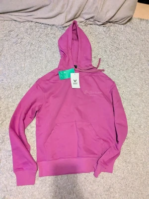 Rosa hoodie - Säljer en snygg rosa hoodie med broderad text. Tröjan har huva med snörning, stor magficka och långa ärmar. Perfekt för chill eller träning. Materialet är mjuk bomull som känns skönt mot huden. Nypris 299☺️