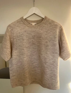 Beige stickad kortärmad tröja - Supermysig beige stickad tröja med korta ärmar och rund hals. Perfekt för lager-på-lager. Mjuk och skön känsla tack vare det stickade materialet. Enkel och clean design som funkar till många olika stilar.