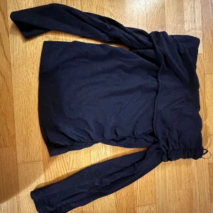 Svart offshoulder långärmad tröja - Snygg svart offshoulder tröja med långa ärmar och en cool snörningsdetalj vid axlarna. Perfekt för dig som vill ha en stilren och trendig look. Materialet känns mjukt och bekvämt mot huden.