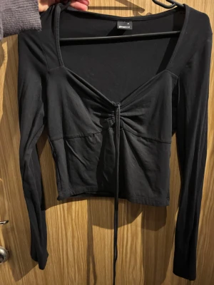 Svart croppad topp med snörning Gina Tricot - Svart långärmad croppad topp från Gina Tricot med snygg snörning framtill som ger en cool v-ringad look. Mjuk och stretchig bomullskvalitet, perfekt att styla med jeans eller kjol. Enkel men trendig design med smickrande passform.
