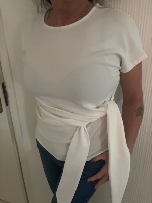 Vit omlottopp med knyt från Anna Field - Supersnygg vit topp från Anna Field med breda omlottband som kan knytas i midjan. Modellen är kortärmad och har en rund halsringning. Helt ny med lapp på. Storlek L men sitter bra på mig som har M