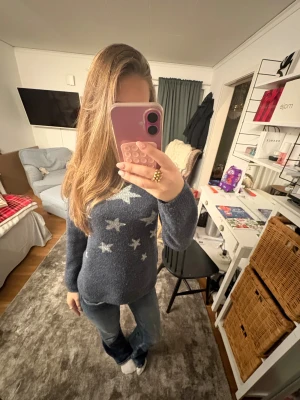 Blå stickad tröja med stjärnor H&M - Mysig blå stickad tröja från H&M med vita stjärnor över hela framsidan. Tröjan har en klassisk rund halsringning och långa ärmar. Perfekt för kyligare dagar och enkel att matcha med jeans eller andra byxor.