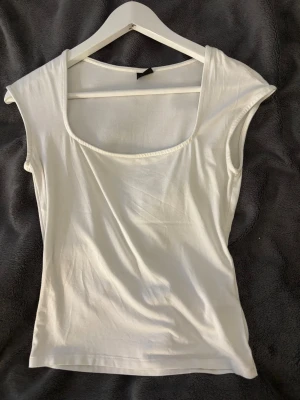 Vit ärmlös linnetopp med breda axlar - Säljer en stilren vit linnetopp med breda axlar och djup rundad halsringning. Toppen är ärmlös och har en enkel, clean design som funkar till många olika looks. Materialet känns mjukt och lätt, perfekt för varma dagar.
