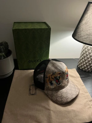 Gucci keps tiger - Snygg Gucci keps i beige och brunt, mesh i svart baktill och broderade tigrar framtill. Låda samt dustbag följer med. 