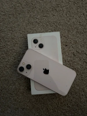 iPhone 13 - Snygg rosa iPhone 13 med originalkartong. Telefonen har dubbla kameror och ser ut att vara i gott skick utan synliga repor eller skador på skärm eller baksida. Perfekt för dig som vill ha en modern och kraftfull mobil med stilren design.