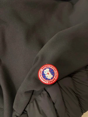 Svart quiltad jacka från Canada Goose - Säljer en svart quiltad jacka från Canada Goose med ribbade muddar och hel dragkedja framtill. Jackan har två fickor med dragkedja och den klassiska Canada Goose-loggan på ärmen. Perfekt för dig som vill ha en stilren och varm jacka med snygg passform.