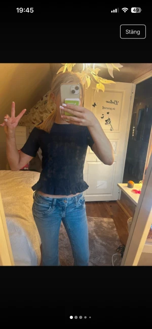 Mörkblå volangblus från Gina Tricot - Supersöt mörkblå blus från Gina Tricot med smockad midja och volangkant nertill. Toppen har korta ärmar och rund halsringning. Materialet är mjukt och stretchigt, perfekt för en chill och trendig look.