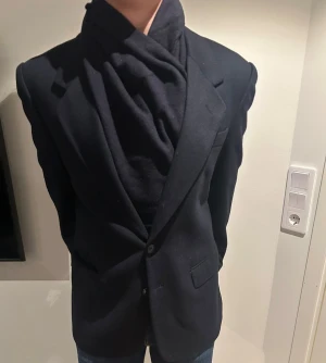 Svart rock från Mario Zegna - Stilren svart rockfrån Mario Zegna, tillverkad i Italien. Klassisk modell med två knappar framtill, breda slag och fickor med lock. Materialet är mjuk ull som ger en exklusiv känsla. Passar dig som vill ha en tidlös och elegant look.
