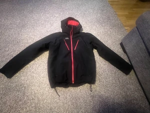 Svart vindjacka från Five Seasons - Svart vindjacka med röd insida och röda dragkedjor från Five Seasons. Jackan har huva med snörning, tre dragkedjeförsedda fickor framtill och justerbar nederkant. Perfekt för kalla och blåsiga dagar, snygg och sportig look.