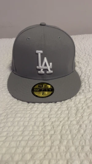Grå LA Dodgers keps från New Era - Snygg grå 59FIFTY keps från New Era med LA Dodgers broderat i vitt framtill. Klassisk flat brim och broderade ventilationshål. MLB-logga baktill och New Era-logga på sidan. Tillverkad i polyester för en clean look.