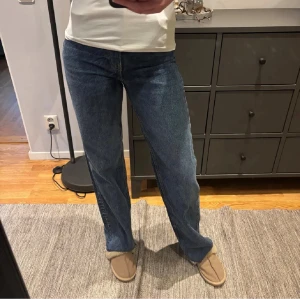 Blå raka jeans från ZARA - Säljer ett par klassiska blå jeans från ZARA med raka ben och normal passform. Jeansen har medel hög midja, knappgylf och fem fickor. Materialet är robust denim i bomull och färgen är en snygg mellanblå tvätt med slitna detaljer vid kanterna.