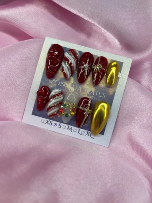 CandySpark (S);Medium Almond - Säljer ett set handgjorda press-on naglar i en medium mandelform med juldesign. Naglarna är röda med glitter, vita ränder, guldrosetter, stjärnor och en vit nagel med färgglada pärlor som julkrans. Två naglar är metallicguld. Perfekt för dig som vill ha extra festliga naglar!