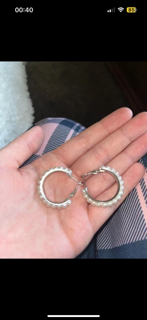 Silverfärgade hoops med pärlor - Säljer ett par snygga örhängen i hoop-modell med silverfärgad bas och vita pärlor längs hela ringen. De har en klassisk rund form och stängs med smidig klick-lås. Perfekta för dig som gillar stilrena detaljer med lite extra bling.