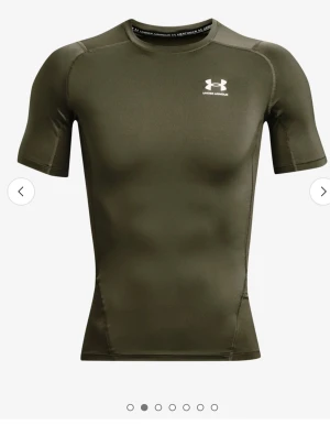 Grön tight t-shirt från Under Armour - Sportig grön t-shirt från Under Armour med korta ärmar och vit logga på bröstet. Modellen är tight och tillverkad i ett stretchigt syntetmaterial som andas, perfekt för träning. Snygg passform som framhäver axlar och armar.