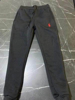 Svarta mjukisbyxor från Polo Ralph Lauren - Svarta mjukisbyxor från Polo Ralph Lauren med röd broderad logga på vänster lår. Byxorna har snörning i midjan, ribbade muddar vid bensluten och mjukt bomullsmaterial. Perfekt passform med normal siluett och fickor på sidorna anledning till salu är att jag beställde den från polo hemsidan och den kom lite tight tack