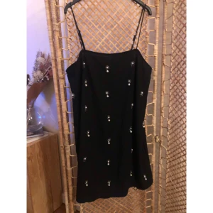 Svart kort klänning med pärldetaljer H&M - Supersnygg svart kort klänning från H&M med tunna axelband och glittriga pärldetaljer över hela klänningen. Perfekt för dig som vill sticka ut med en elegant men cool look. Klänningen har en rak passform och är ärmlös.