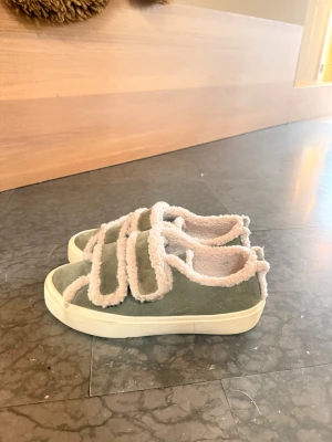 Gröna Inuikii sneakers med fuskpäls - Unika sneakers från Inuikii i grön mocka med fluffiga beige detaljer och kardborreband. Skorna har en platt vit sula och är fodrade med mjuk fuskpäls för extra komfort. Ny pris 2600kr