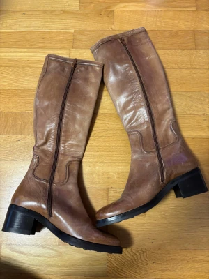 Brun läderstövel med dragkedja och låg klack storlek 37 - Snygga bruna stövlar i skinn med rund tå och låg klack. De har dragkedja på sidan och robust sula med bra grepp. Perfekta för dig som gillar klassisk stil med en modern touch. Passar till både jeans och kjol. Storlek 37 riktigt läder 