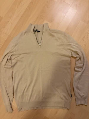 Beige half zip tröja Only & Sons - Snygg beige långärmad tröja från Only & Sons med half zip-dragkedja i halsen. Tröjan har en stilren design med ribbade muddar och är tillverkad i mjukt material som känns skönt mot huden. Perfekt för dig som gillar enkel och clean stil.