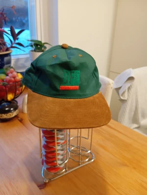 Ny Grön BEE keps med brun manchester-skärm - Ny grön keps från BEE med broderad logga framtill och en bred, brun skärm i mjuk manchester. Kepsen har bruna detaljer på toppen och ventilationshål, vilket ger en retro och chill vibe. Perfekt för dig som vill sticka ut med en unik accessoar.