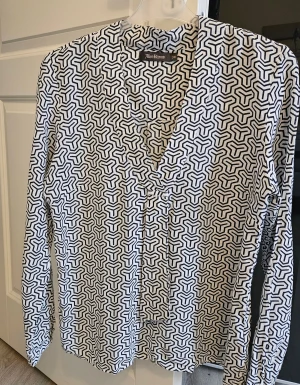 Mönstrad skjorta från Alice Bizous - Svart och vit långärmad blus med ett geometriskt mönster. Blusen har en v-ringning och knäppning framtill.