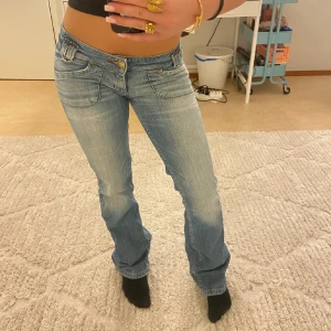 Lågmidjade bootcut jeans i ljusblå denim - Snygga lågmidjade jeans från Lee i ljusblå denim med bootcut passform. Jeansen har dekorativa fickor med knappar bak och coola detaljer vid midjan 💗. W28 L33