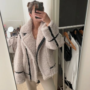 Beige teddyjacka med svarta detaljer - Säljer en oversized beige teddyjacka med svarta detaljer och dragkedja. Jackan är supermjuk med fluffig textur. Perfekt för dig som vill ha en mysig och trendig look under kyliga dagar. Jackan är från H&M i storlek S. Den är helt ny och aldrig använd💞