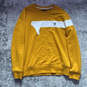 Gul sweatshirt från G-Star RAW - Cool gul sweatshirt från G-Star RAW med vit grafisk detalj över bröstet och logga. Tröjan har rund halsringning och långa ärmar. Perfekt för dig som vill sticka ut med en färgstark och bekväm stil.
