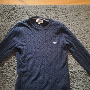 Marinblå kabelstickad tröja Hampton Republic - Kabelstickad marinblå tröja från Hampton Republic med rund halsringning och diskret logga broderad på bröstet. Långärmad och klassisk modell som är perfekt för lager-på-lager. Snygg ribbad kant vid halsen.