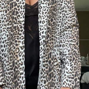 Leopardmönstrad kappa som går att knäppa på och ser ut som en klänning  - Snygg lång overshirt med leopardmönster i beige, svart och brunt. Jackan har knappar framtill och raka ärmar. Perfekt statement-plagg för dig som vill sticka ut och addera lite edge till din outfit.