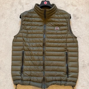 Olivgrön dunväst från Colmar - Snygg olivgrön dunväst från Colmar med quiltad design och hög krage. Västen har två dragkedjeförsedda fickor framtill och Colmar-logga på bröstet samt på baksidan längre ned. Perfekt för lager-på-lager och enkel att matcha med hoodies eller tröjor. Har ett lagat hål som man knappast märker. Nypris ligger på ca 2000, pris kan diskuteras.