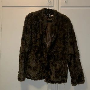 Brun pälsjacka från H&M Divided - Mysig brun pälsjacka från H&M Divided med mjukt foder och klassisk rak passform. Jackan har lång ärm och är tillverkad i syntetmaterial som ger en fluffig och lyxig känsla. Perfekt för att hålla värmen under kyliga dagar.