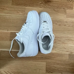 Nike Air Force 1 vita sneakers - Klassiska helvita Nike Air Force 1 sneakers med låg profil. Skorna har snörning, perforerad tå och är tillverkade i skinn. Perfekta för en clean och stilren look, passar till det mesta i garderoben.