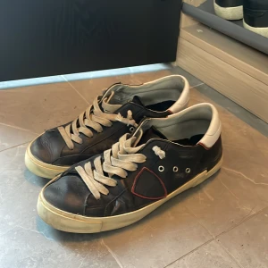 Svarta sneakers med vit sula - Svarta sneakers med vit sula och vita skosnören. Skorna har en kontrasterande vit hälkappa och en röd detalj på sidan. Klassisk rund tå och lågt skaft, perfekt för en avslappnad streetstil.