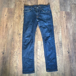Nudie Jeans Lean Dean 33/34 - Snygga mörkblå jeans från Nudie Jeans med klassisk femficksdesign och kontrastsömmar. Modellen har raka ben och normal passform. Bakfickorna har Nudie Jeans signaturbroderi i ljusblått. Perfekta för dig som gillar stilrena och tidlösa jeans. Modellen heter lean Dean och de är i storlek 33/34