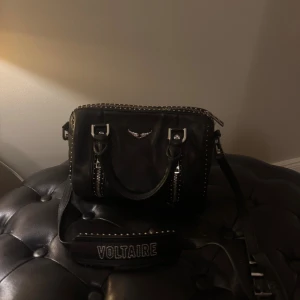 Svart Zadig & Voltaire handväska i skinn - Cool svart handväska från Zadig & Voltaire, dubbla dragkedjor och bred axelrem med logga. 