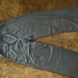Blå satinpants från Vero Moda S - Snygga blå satinpants från Vero Moda i storlek S. Byxorna har elastisk midja med snörning och är tillverkade i ett glansigt, mjukt material som ger en chill och trendig look. Perfekta för dig som gillar bekväma men stilrena byxor. Lite uppsprätt vid insidan av höften men ingenting som påverkar så mycket.
