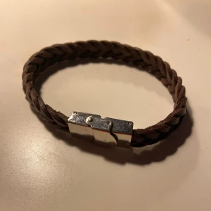 Brunt flätat läderarmband med metallspänne - Snyggt armband i brunt flätat läder med ett stilrent silverfärgat metallspänne. Perfekt accessoar för dig som gillar en enkel men cool look. Oanvänd köpt i Kroatsien💕