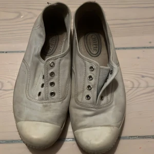 Vita sneakers från Chipie - Säljer ett par klassiska vita sneakers från Chipie med gummitå och sula. Skorna är i bomullstyg och har metallöljetter för snörning, men levereras utan skosnören. Märkeslogga med hund på hälen. Perfekta för en chill och enkel stil.