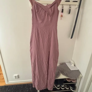 Lång rosa klänning med v-ringning - Säljer en lång, ärmlös klänning i en mjuk rosa nyans. Klänningen har en snygg v-ringning framtill och en slits framtill för extra rörelsefrihet. Materialet känns lätt och passar perfekt till varmare dagar. Dragkedja baktill för enkel påklädning.