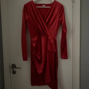 Röd omlottklänning från Bubbleroom - Snygg röd omlottklänning från Bubbleroom i glansigt material. Har använts en gång, klänningen har lång ärm, v-ringning och ett knytband i midjan som ger en smickrande siluett. Perfekt för dig som vill sticka ut med en elegant look.