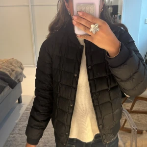 Svart quiltad pufferjacka från BOSS - En knapp som har gått av men syns inte. Svart pufferjacka från BOSS med quiltad design och rundad krage. Jackan har knäppning framtill, ribbade muddar och en stilren look. Tillverkad i syntetmaterial och passar perfekt för kyligare dagar. Snygg och enkel att matcha med allt. 🥰🥰