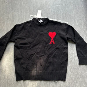 Svart stickad tröja amiri  - Svart stickad tröja från Ami Paris med rund halsringning och ribbade muddar. På bröstet finns ett rött hjärta med bokstaven A, helt ny