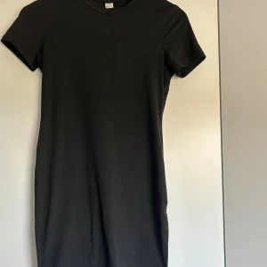 Svart t-shirtklänning från SHEIN - Enkel svart t-shirtklänning från SHEIN med rund halsringning och korta ärmar. Modellen är rak och slutar ovanför knäna. Perfekt basplagg som är lätt att styla med sneakers eller boots. Gjord i mjukt material för en bekväm känsla.