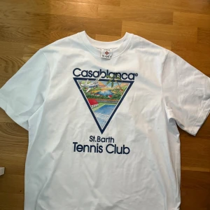 Vit Casablanca Tennis Club t-shirt - Vit t-shirt från Casablanca med stort färgglatt tryck och texten 'St. Barth Tennis Club' på bröstet. Klassisk passform, rund hals och korta ärmar. Tillverkad i mjuk bomull, perfekt för en sportig och trendig look.