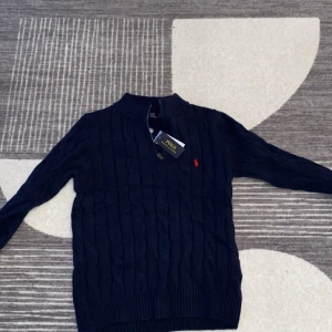 Mörkblå kabelstickad tröja Polo Ralph Lauren - Kabelstickad mörkblå tröja från Polo Ralph Lauren i 100% bomull. Klassisk modell med rund hals, ribbade muddar och röd broderad logga på bröstet. Perfekt för dig som gillar stilren och tidlös design. Passar både S/M. Pris kan diskuteras vid snabbaffär!!