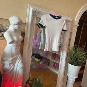 Zara Top Tee - Vit ribbad topp från Zara med marinblå kant vid halsringning och ärmslut. T-shirten har en klassisk passform och är tillverkad i mjuk bomull. Perfekt att styla med jeans eller kjol för en clean look.