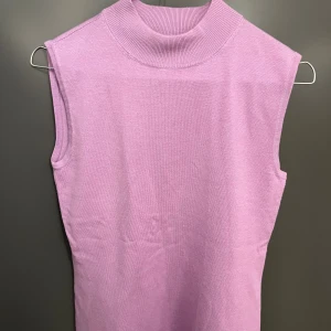 Ljuslila stickad polotopp från Wico - Säljer en ljuslila stickad polotopp från Wico. Toppen är ärmlös med en hög ribbad krage och har en clean, minimalistisk look. Perfekt att styla med jeans eller kjol för en trendig vibe.