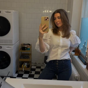 Vit skjorta med puffärm - Vit skjorta i bomull med trendiga puffärmar och dold knäppning framtill. Modellen har en rak passform och trekvartsärm som ger en cool och modern vibe. Perfekt att styla med jeans eller kjol för en clean look.