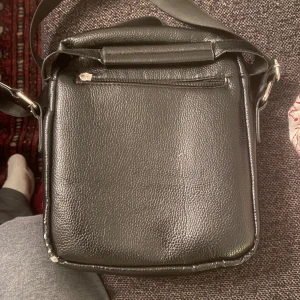 Boss man väska mindre modellen  - En läderväska för men i okej skick av kvalitet märket Hugo boss och det finns även både fler fickor och en medalplatta med loggan på två olika platser i väskan den går å snygga till utan att betala mer än å i ordning ställa den men läder nästan inget att klaga på normal slitage. 